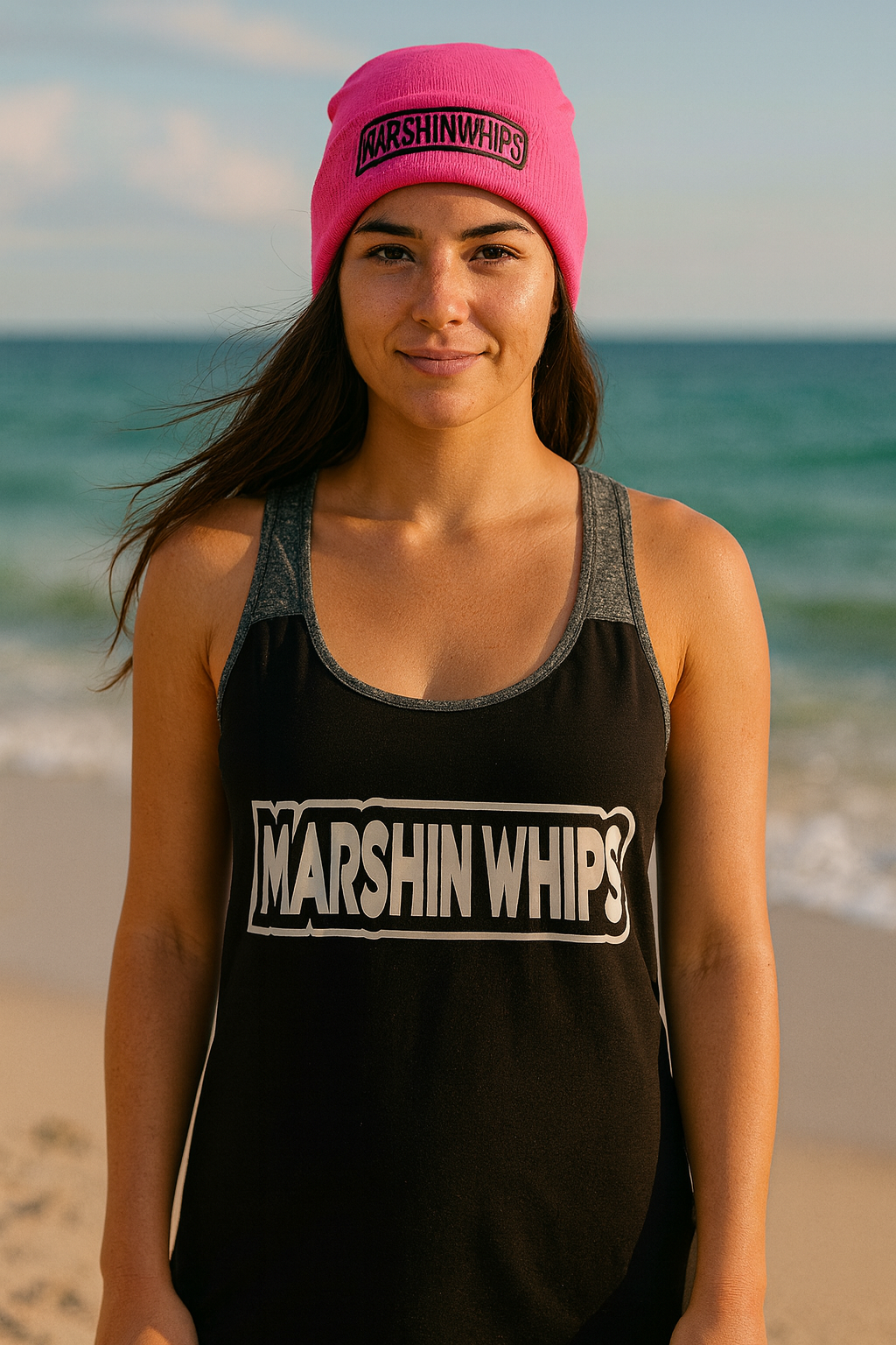 Woman wearing a black tank top and pink beanie with 'MARSHIN WHIP' branding on a beach.
