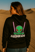Person wearing a black hoodie with an alien graphic and 'Marshin Whips' text in a desert setting