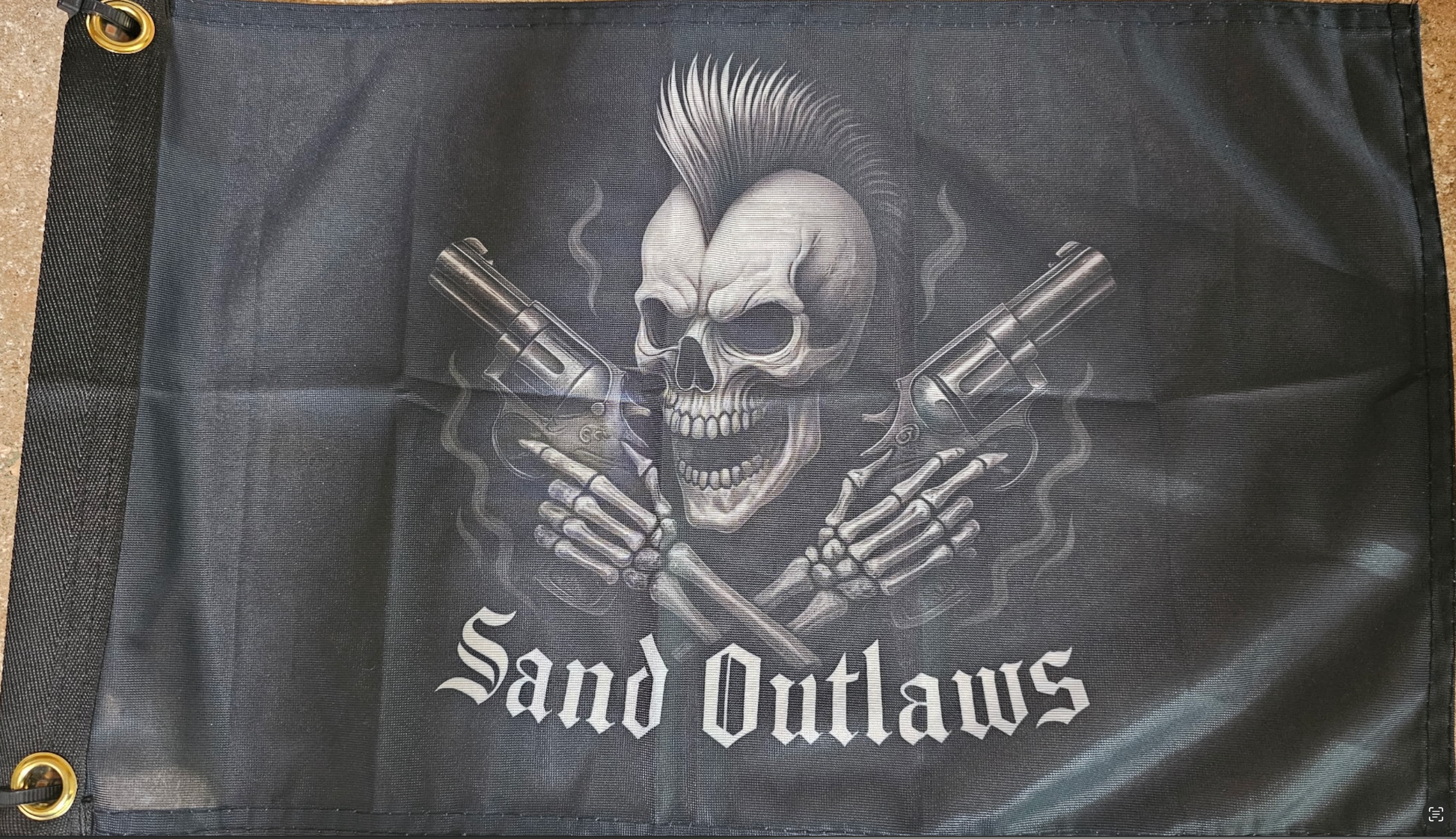Flag with a skull holding guns and 'Sand Outlaws' text on a dark background