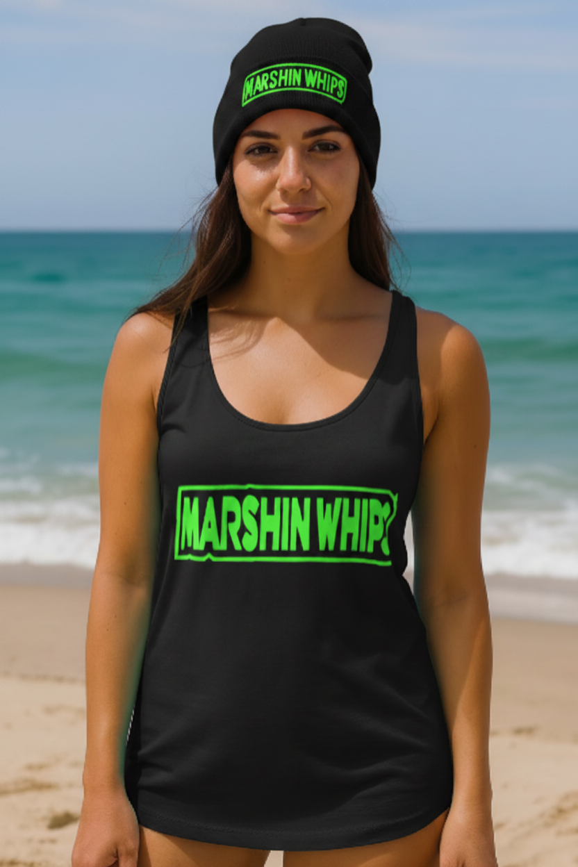Woman wearing a black tank top and pink beanie with 'Marshin Whips' branding on a beach.