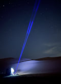 Blue laser pointer beam against a night sky with trees