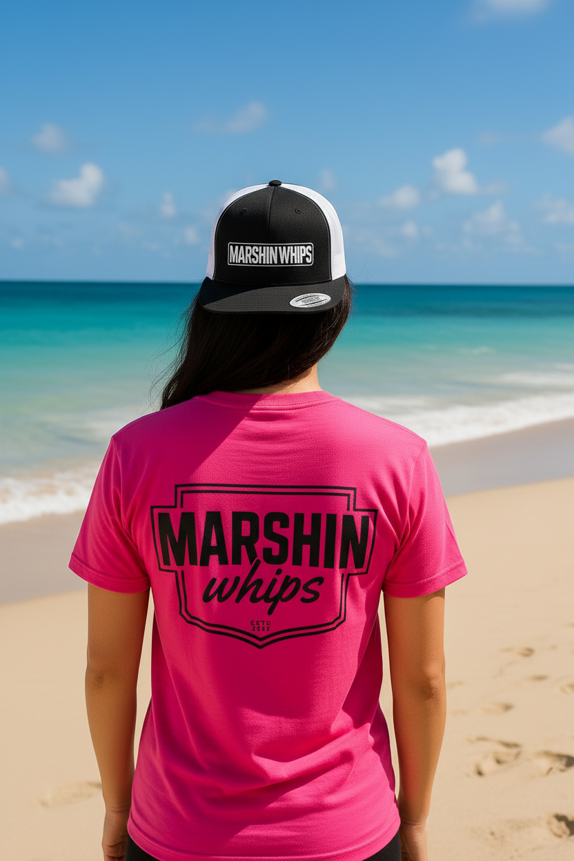 Person wearing a pink t-shirt and cap with 'Marshin Whips' branding on a beach.