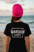 Person wearing a black t-shirt with 'MARSHIN whips' logo and a pink beanie on a beach.