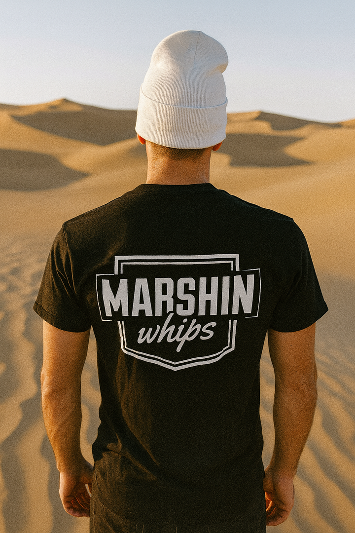 Person wearing a black t-shirt with 'MARSHIN whips' logo in a desert setting