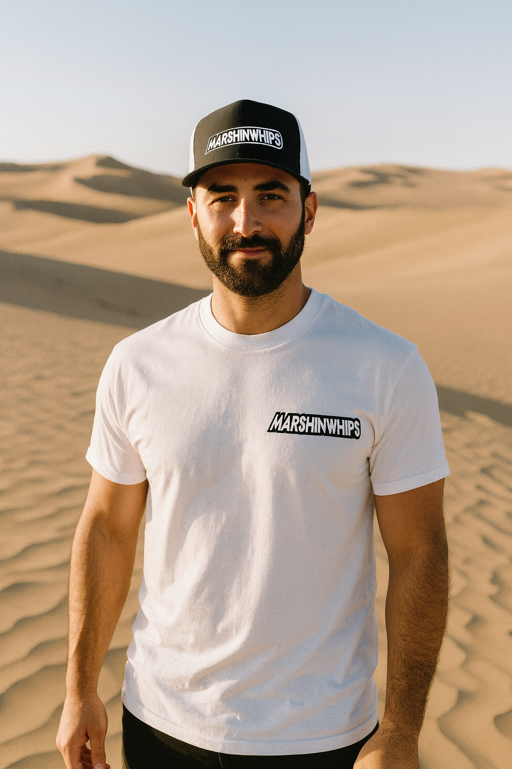 Man wearing a white t-shirt and black cap with 'Marshin whips branding in a desert setting